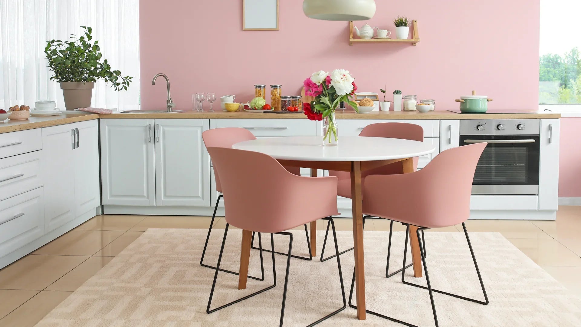 Açık tonlarda modern geometrik desenli halı, pembe sandalyeli mutfak masası altında serili.
